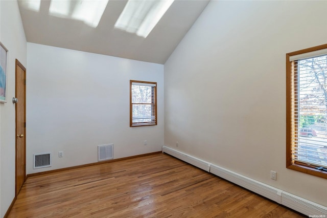 spare room featuring light hardwood / wood-style floors, vaulted ceiling, and a baseboard heating unit