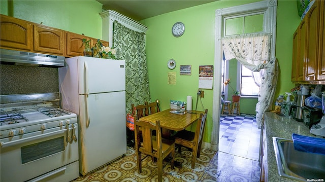 kitchen with under cabinet range hood, light floors, brown cabinets, white appliances, and a sink