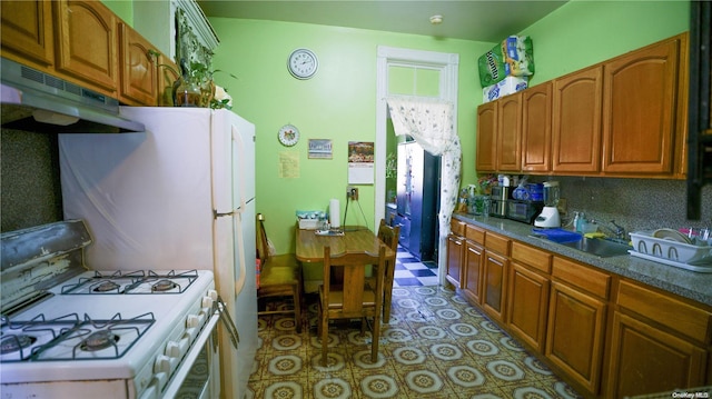 kitchen with light tile patterned floors, white gas range, a sink, under cabinet range hood, and brown cabinets