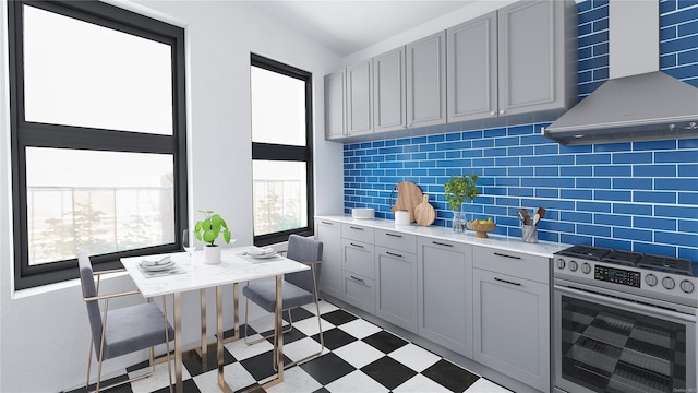 kitchen featuring stainless steel gas stove, gray cabinets, wall chimney range hood, light countertops, and light floors