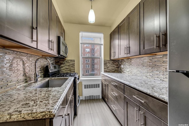 kitchen featuring dark brown cabinetry, sink, decorative light fixtures, radiator, and stainless steel appliances