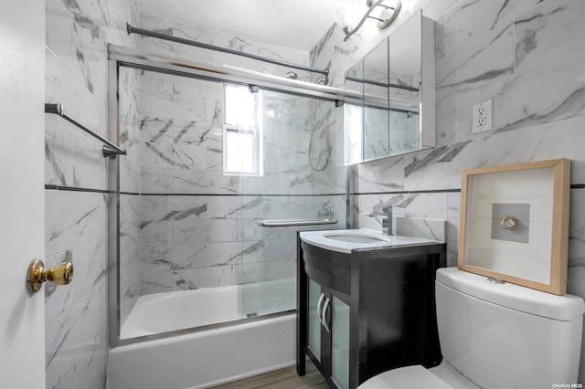 full bathroom featuring toilet, vanity, shower / bath combination with glass door, and tile walls