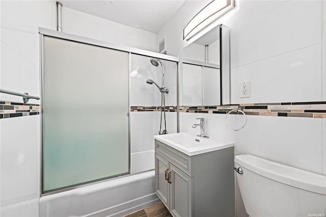 full bathroom featuring vanity, toilet, tile walls, and bath / shower combo with glass door