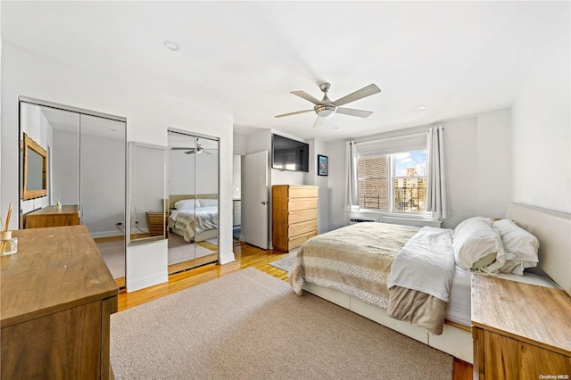 bedroom featuring ceiling fan, light hardwood / wood-style floors, and two closets