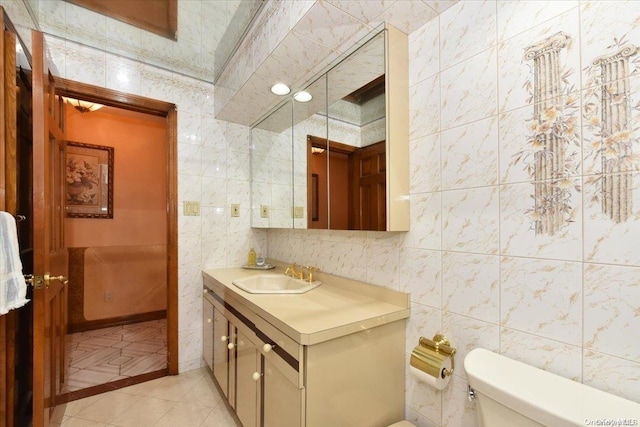 bathroom with toilet, vanity, tile patterned floors, and tile walls