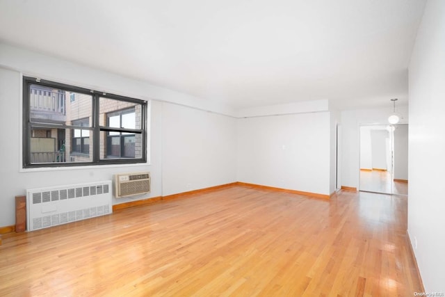 unfurnished living room with hardwood / wood-style floors, an AC wall unit, and radiator