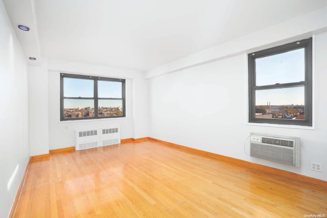 unfurnished room with a wall mounted AC, hardwood / wood-style flooring, and radiator