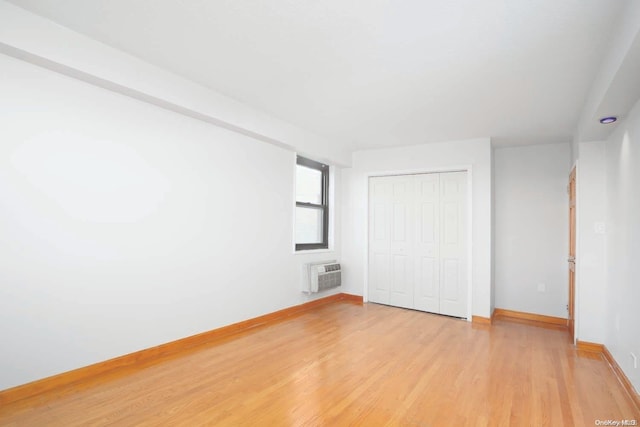 unfurnished bedroom featuring light hardwood / wood-style flooring, a wall unit AC, and a closet