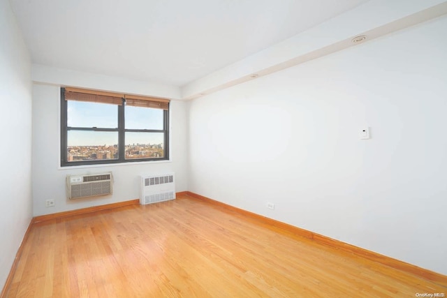 unfurnished room featuring radiator heating unit, an AC wall unit, and hardwood / wood-style floors