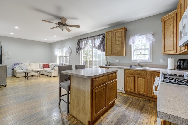 kitchen featuring dark wood-type flooring, a breakfast bar, sink, a center island, and white appliances