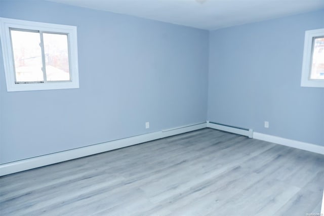 unfurnished room with light wood-type flooring, a wealth of natural light, and a baseboard heating unit