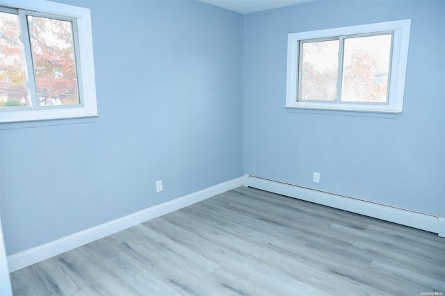 empty room with baseboard heating, a wealth of natural light, and light hardwood / wood-style floors