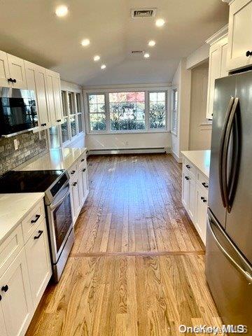 kitchen with tasteful backsplash, stainless steel appliances, baseboard heating, light hardwood / wood-style flooring, and white cabinets