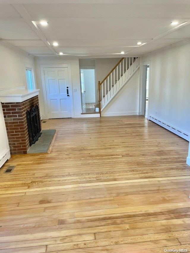 unfurnished living room with a brick fireplace, baseboard heating, and light hardwood / wood-style flooring