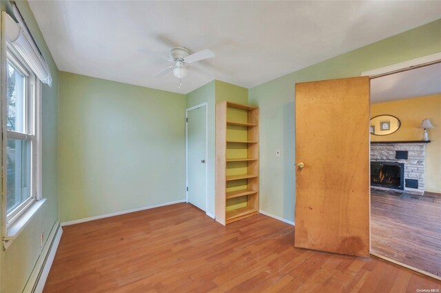 43 2nd St, Ronkonkoma, NY 11779 - unfurnished bedroom featuring a baseboard heating unit, a stone fireplace, wood finished floors, baseboards, and a ceiling fan