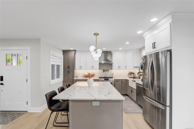 kitchen featuring pendant lighting, a breakfast bar area, wall chimney exhaust hood, a kitchen island, and stainless steel appliances