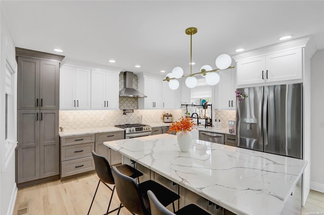 kitchen with appliances with stainless steel finishes, backsplash, wall chimney range hood, decorative light fixtures, and light hardwood / wood-style floors