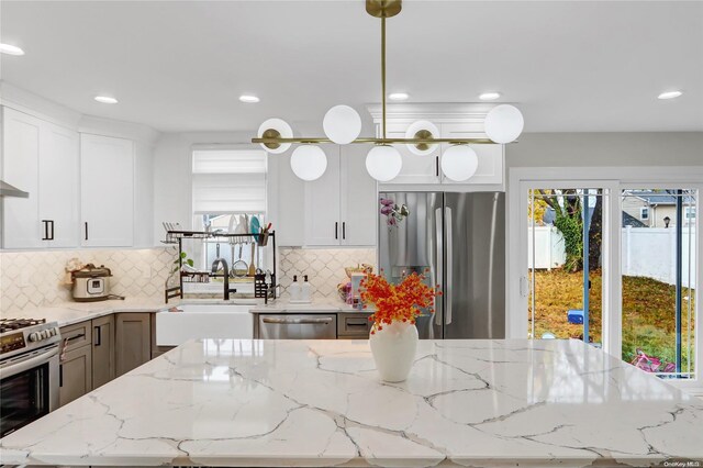 kitchen featuring pendant lighting, light stone counters, white cabinetry, and stainless steel appliances