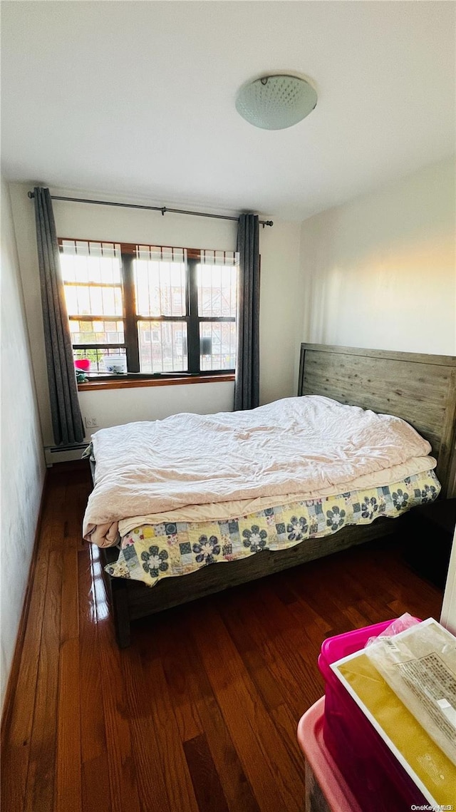 bedroom with dark hardwood / wood-style flooring, baseboard heating, and multiple windows