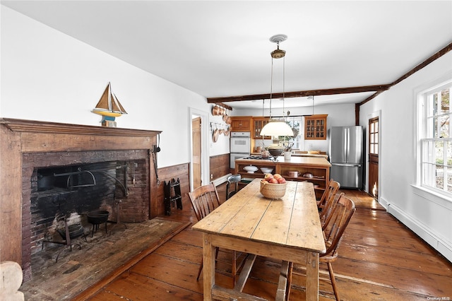 dining area featuring a brick fireplace, beam ceiling, dark wood-type flooring, and baseboard heating