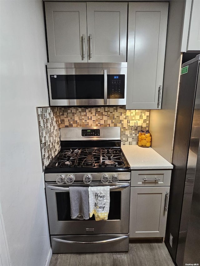 kitchen with decorative backsplash, stainless steel appliances, dark hardwood / wood-style floors, and gray cabinetry