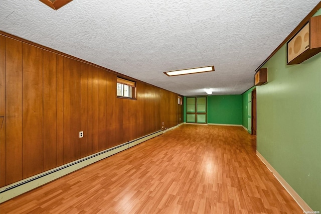 basement with a textured ceiling, a baseboard radiator, light hardwood / wood-style flooring, and wood walls