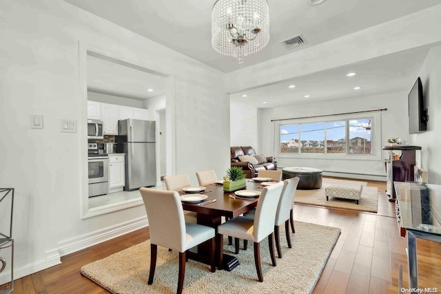 dining room with light hardwood / wood-style flooring, baseboard heating, and a notable chandelier