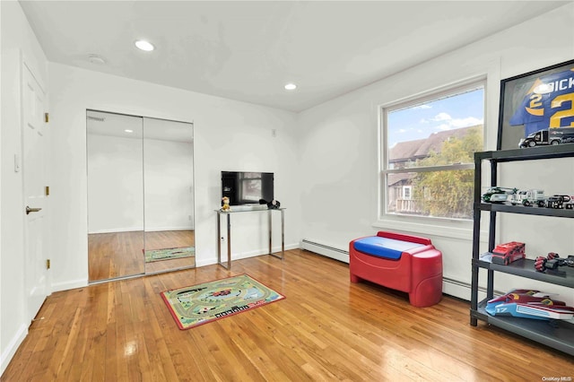 workout room featuring light wood-type flooring and a baseboard heating unit