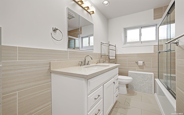 full bathroom featuring shower / bath combination with glass door, vanity, toilet, and tile walls