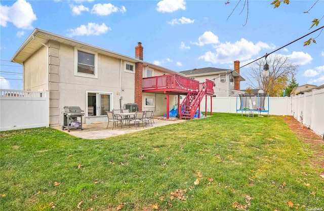 back of property featuring a deck, a trampoline, a patio, and a yard