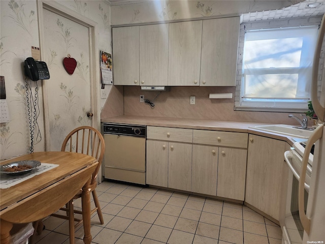 kitchen with light tile patterned floors, white appliances, a sink, light countertops, and wallpapered walls