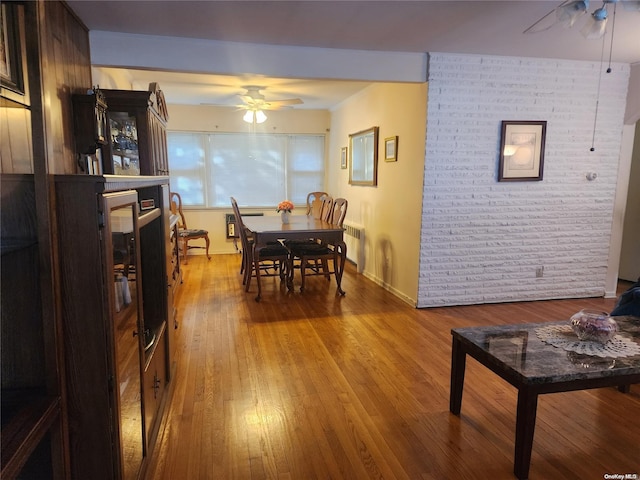 dining area with ceiling fan, brick wall, wood finished floors, baseboards, and radiator