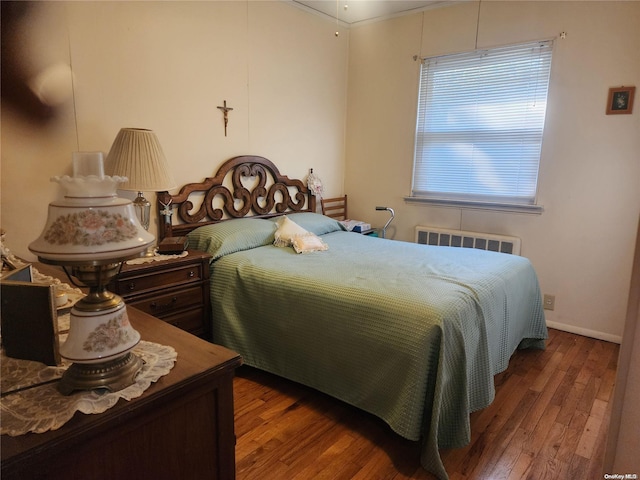 bedroom with radiator heating unit, wood-type flooring, and baseboards