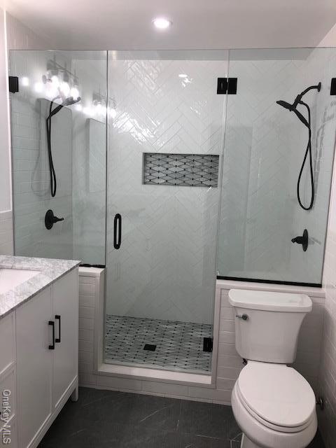 bathroom featuring vanity, a shower with door, tile walls, tile patterned flooring, and toilet