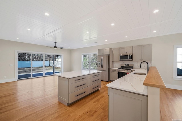 kitchen featuring appliances with stainless steel finishes, light wood-type flooring, light stone counters, gray cabinetry, and sink