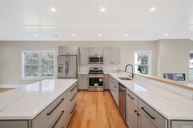 kitchen with kitchen peninsula, stainless steel appliances, sink, light hardwood / wood-style flooring, and gray cabinets