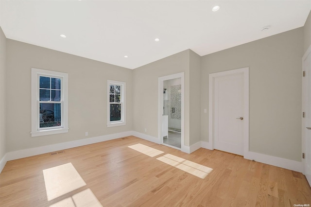 unfurnished bedroom with light wood-type flooring, connected bathroom, and multiple windows