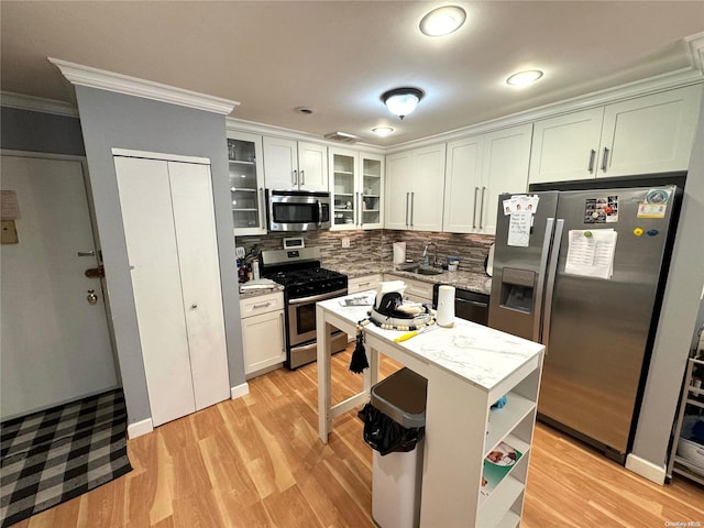 kitchen featuring decorative backsplash, light stone counters, ornamental molding, stainless steel appliances, and light hardwood / wood-style floors