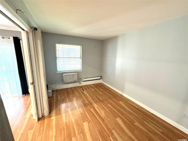 spare room with a wall mounted air conditioner, wood-type flooring, and baseboard heating