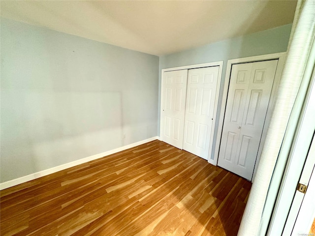 unfurnished bedroom with hardwood / wood-style floors and two closets