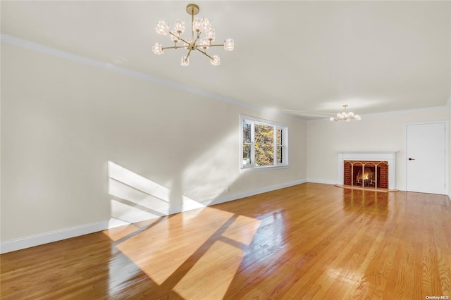 unfurnished living room featuring a brick fireplace, hardwood / wood-style floors, ornamental molding, and a notable chandelier