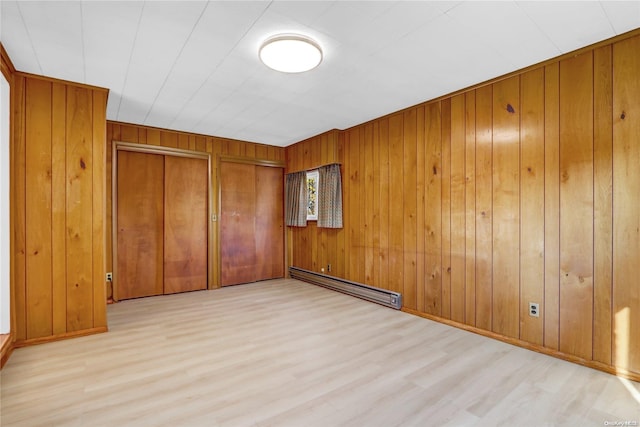 unfurnished room with wood walls, light hardwood / wood-style flooring, and a baseboard radiator