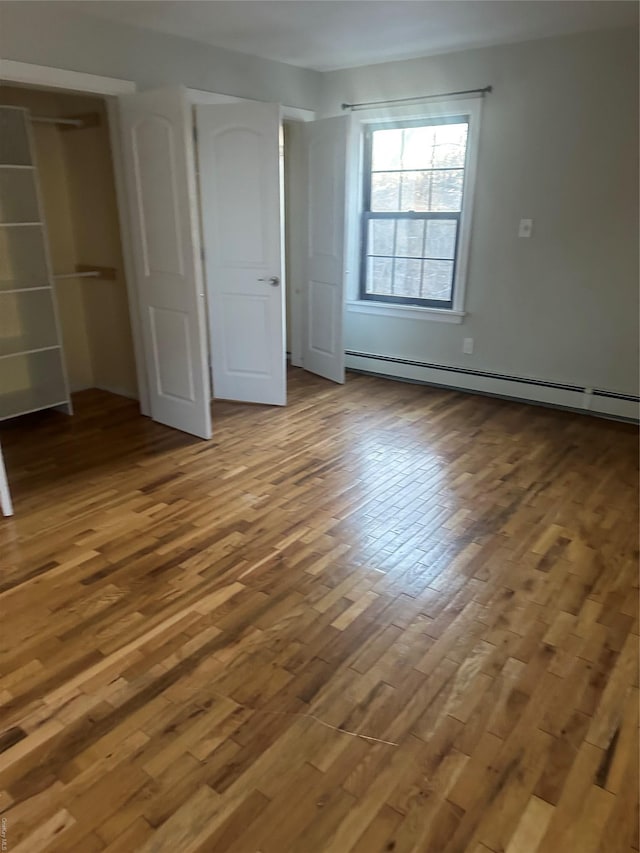 unfurnished bedroom featuring hardwood / wood-style flooring, a closet, and a baseboard heating unit