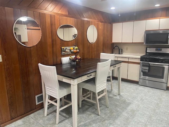 kitchen with wood walls, white cabinets, and appliances with stainless steel finishes