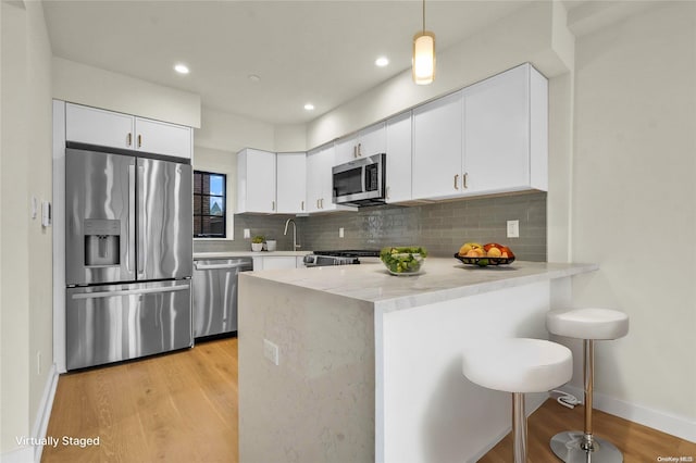 kitchen featuring light wood-type flooring, backsplash, stainless steel appliances, white cabinets, and hanging light fixtures