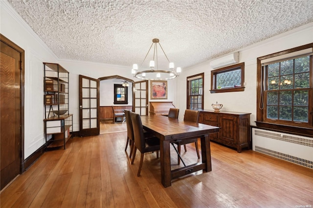 dining area with radiator heating unit, french doors, a wall unit AC, a textured ceiling, and light wood-type flooring