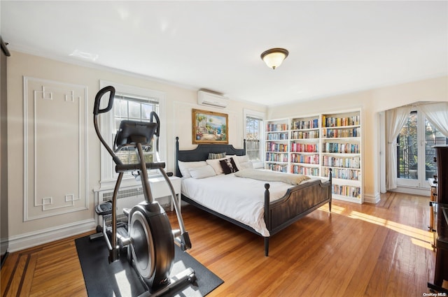 bedroom featuring wood-type flooring, a wall unit AC, and ornamental molding