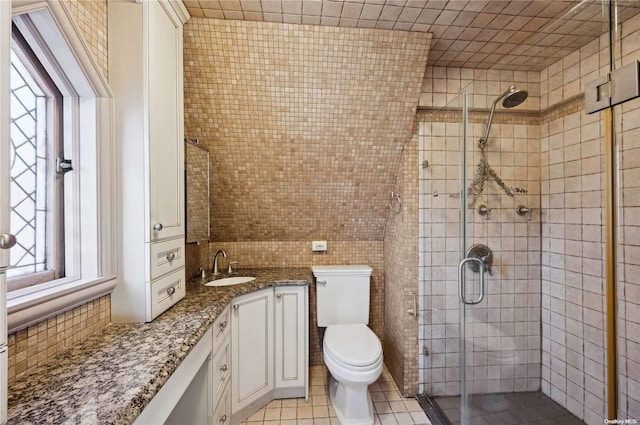 bathroom featuring tile patterned flooring, an enclosed shower, toilet, vanity, and tile walls