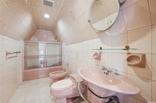 bathroom featuring a bidet, combined bath / shower with glass door, vaulted ceiling, toilet, and tile walls