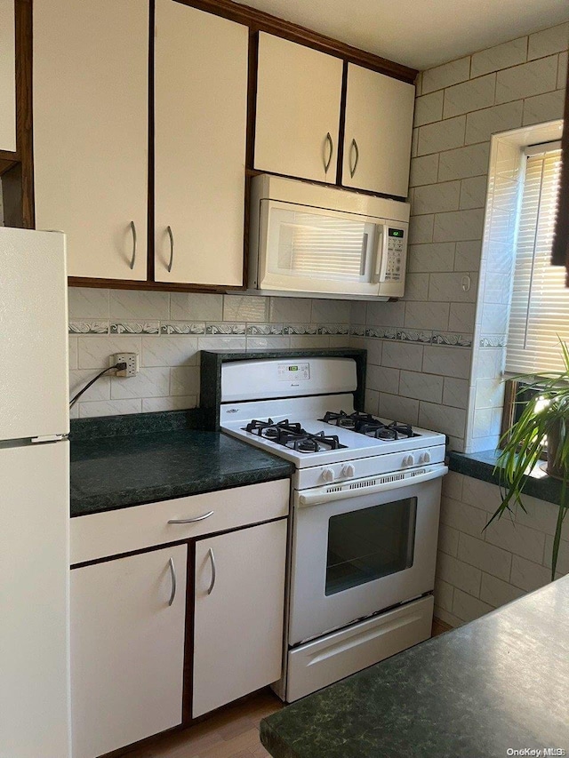 kitchen with white appliances, white cabinetry, and tile walls